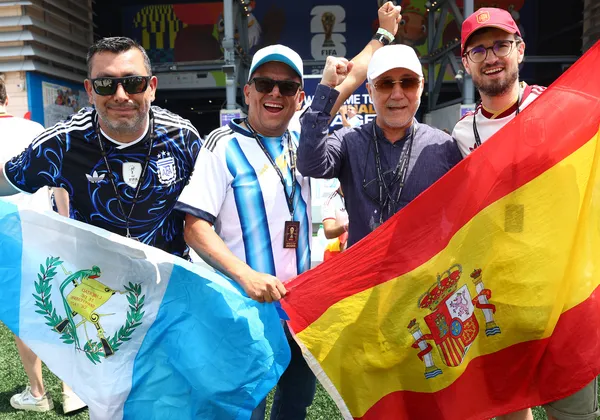 Four fans stand in front of the stadium, holding Argentina and Spain flags