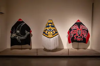 Three Indigenous-made robes lined up in a row in an exhibit.