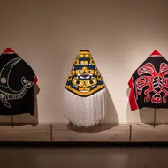 Three Indigenous-made robes lined up in a row in an exhibit.