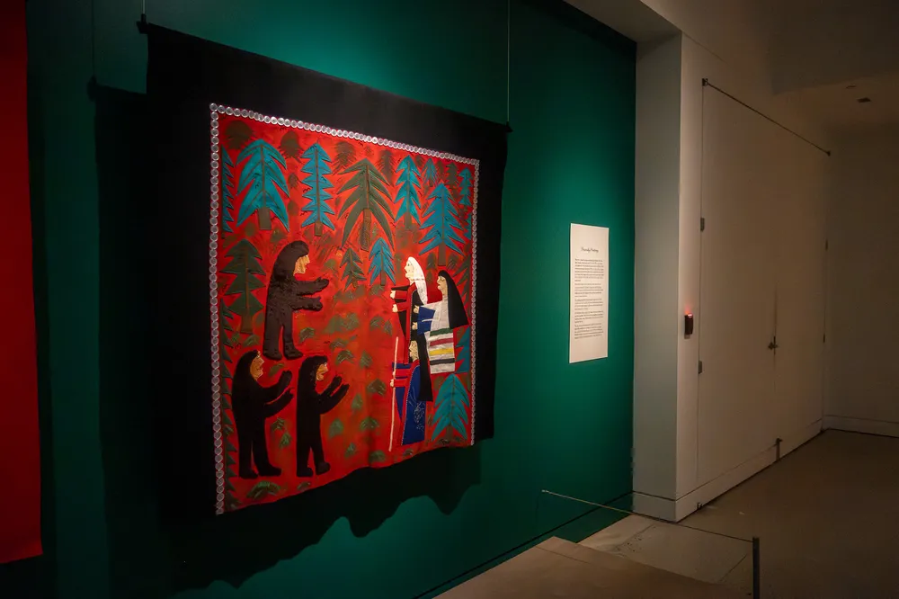 An Indigenous-made robe which depicts three women speaking to three creatures hangs on the wall of an exhibit.