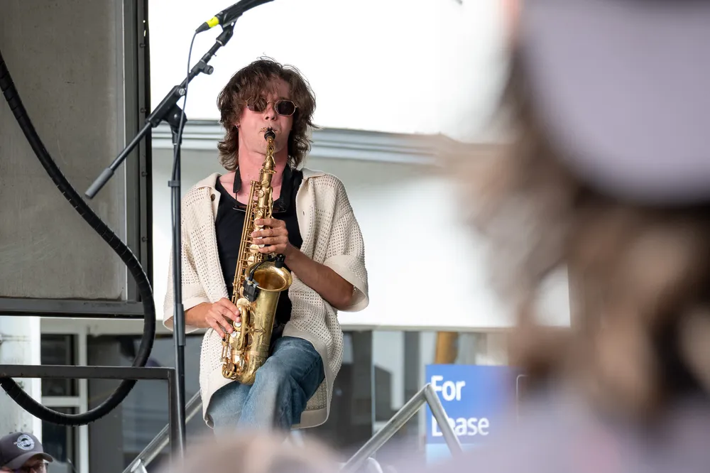 A man with curly hair plays a saxophone on stage.