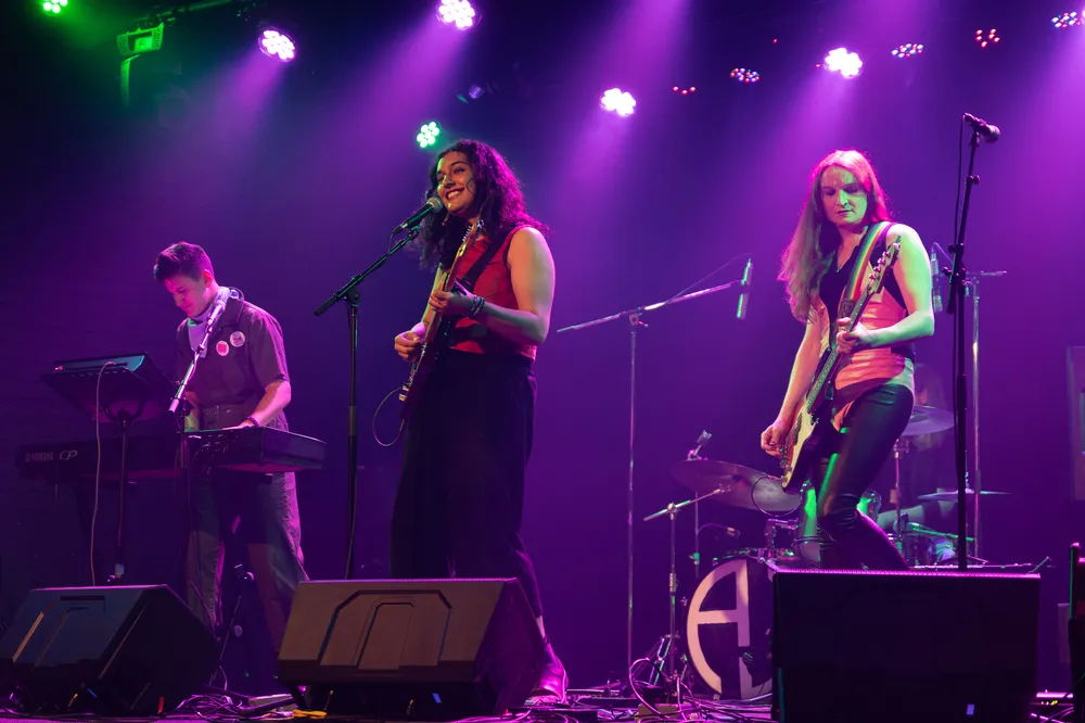 Three band members perform under purple lights