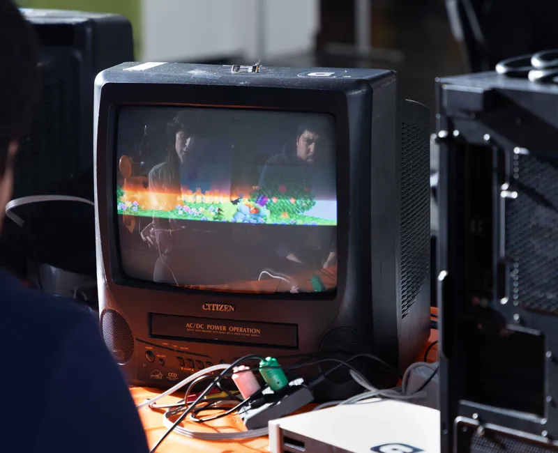 Two people's faces are reflected in the glass of a screen as they play a retro video game.