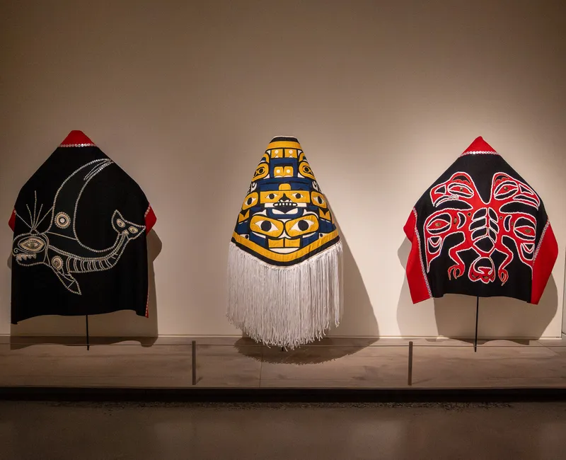 Three Indigenous-made robes lined up in a row in an exhibit.