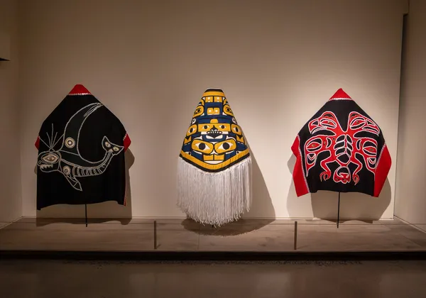 Three Indigenous-made robes lined up in a row in an exhibit.