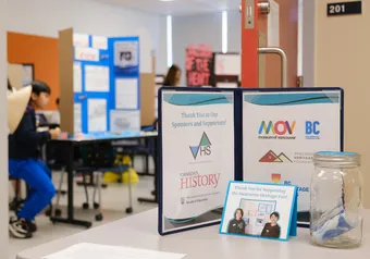 A folder, with a student at a heritage fair poster board in the background