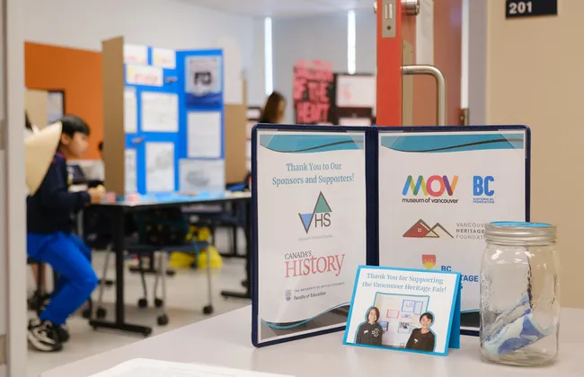 A folder, with a student at a heritage fair poster board in the background