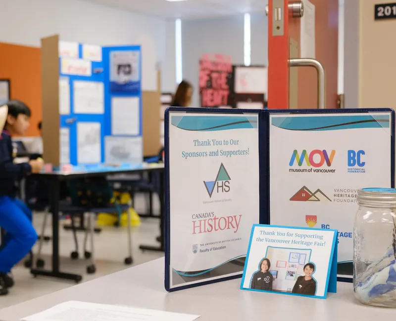 A folder, with a student at a heritage fair poster board in the background