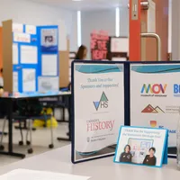 A folder, with a student at a heritage fair poster board in the background