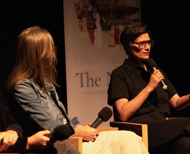Three people sitting on a stage. One holds a microphone and gestures as if speaking.