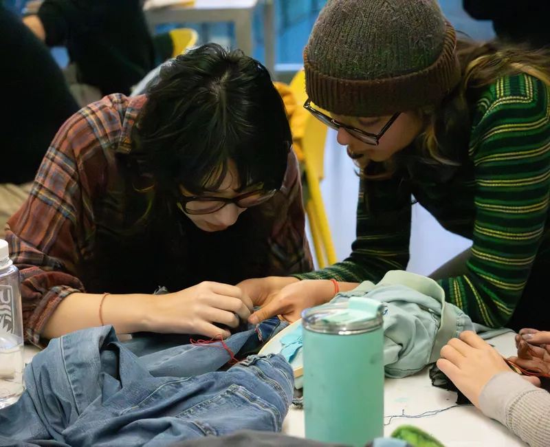 Two people bend over a table mending an item of clothing.