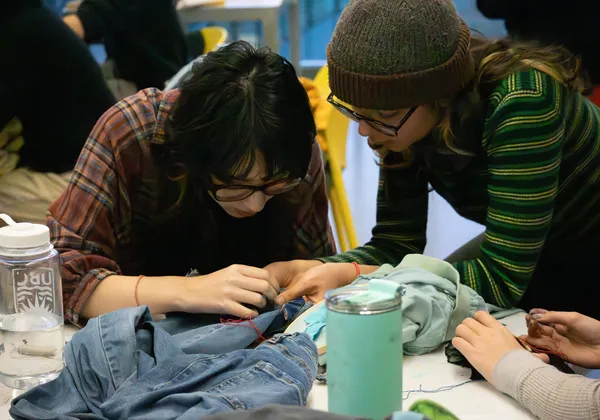 Two people bend over a table mending an item of clothing.
