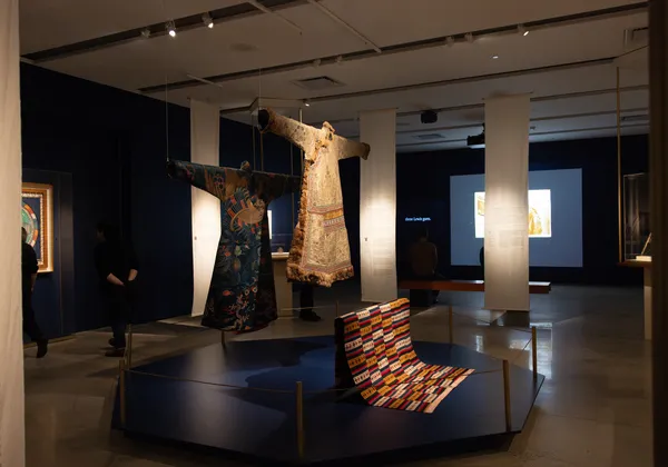 Two robes hang next to a patterned piece of fabric in a museum exhibition