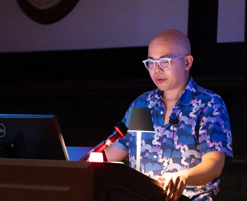 Jade Yumang stands at a podium wearing a blue shirt.