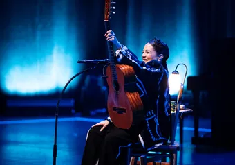 A woman on stage holds an acoustic guitar aloft