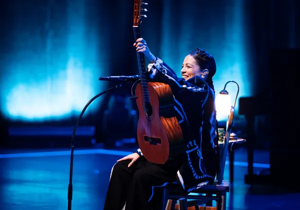 A woman on stage holds an acoustic guitar aloft