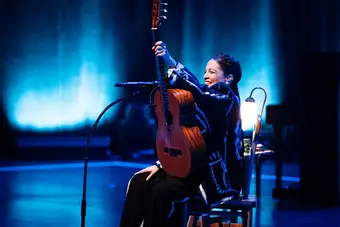 A woman on stage holds an acoustic guitar aloft