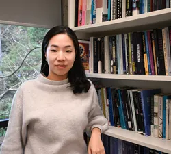 Ji-yoon An, a woman with shoulder-length black hair wearing a grey sweater, stands in front of a bookshelf.