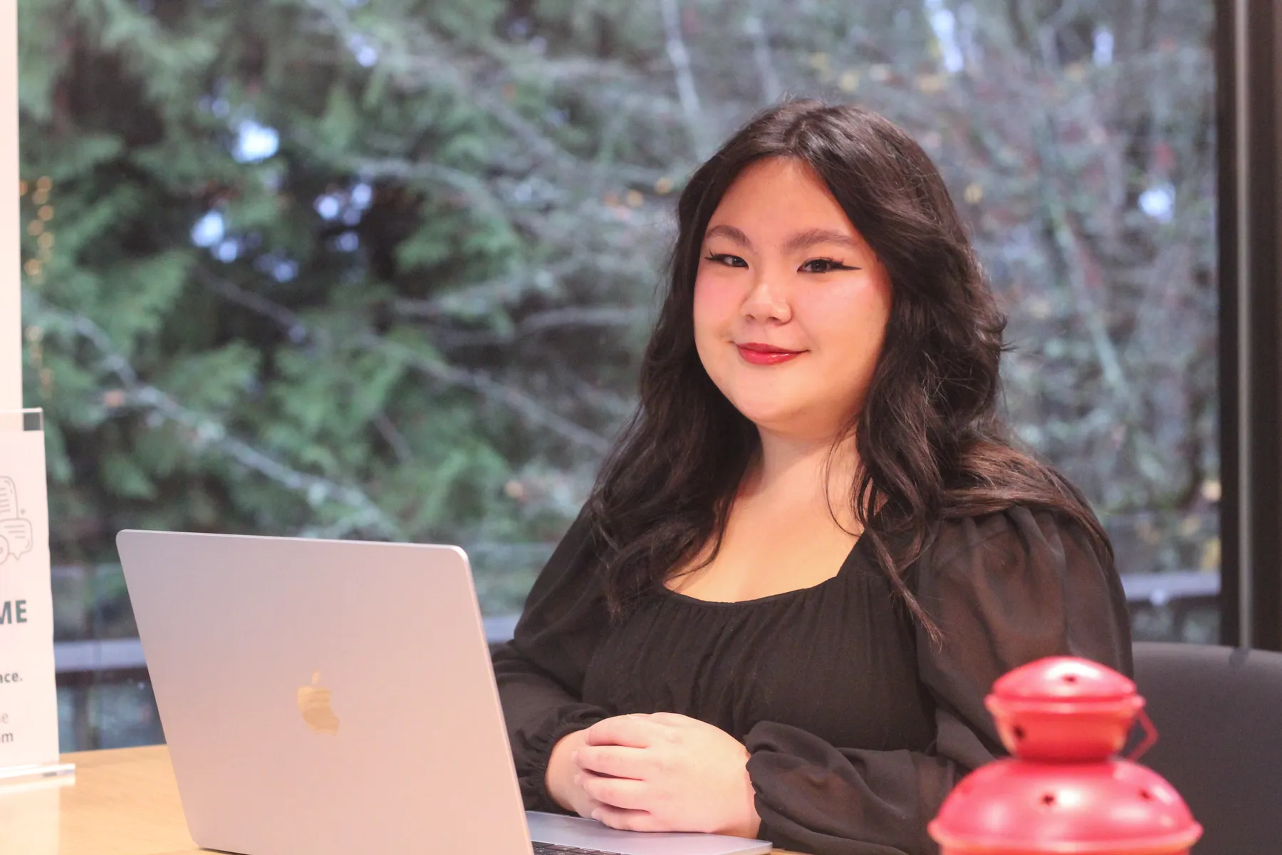 Emily Tang, a Chinese woman with long black hair and a black blouse, smiles while sitting at a table with a laptop in front of her.
