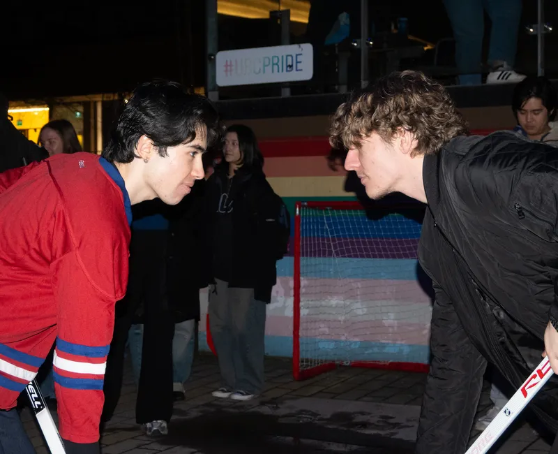 Two contestants face off, holding hockey sticks in front of a net on campus.