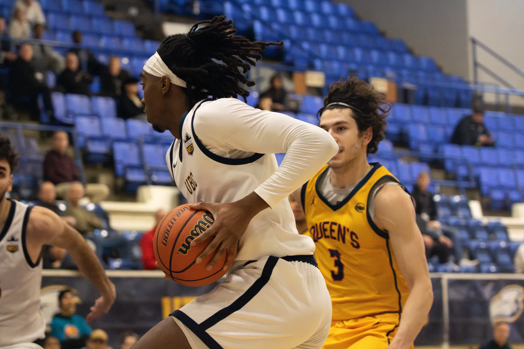 A male basketball player in a white jersey kit holds the ball in his hands, driving to the net.