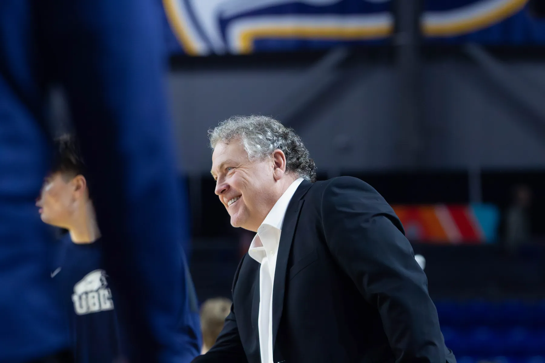 A shot of Kevin Hanson smiling during a team warm-up. He is wearing a white dress shirt and a black suit jacket.
