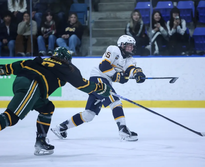 Pursued by an Alberta player in black and green, a UBC player in white and blue takes a shot