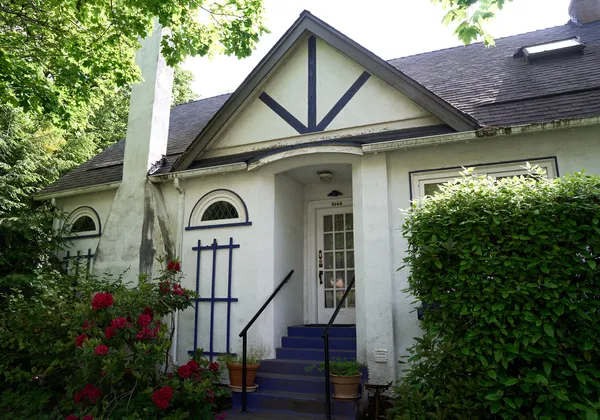 A tan house surrounded by green hedges.