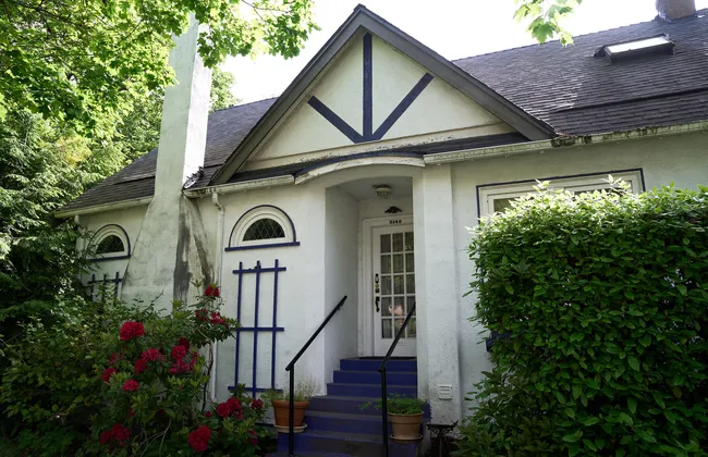 A tan house surrounded by green hedges.