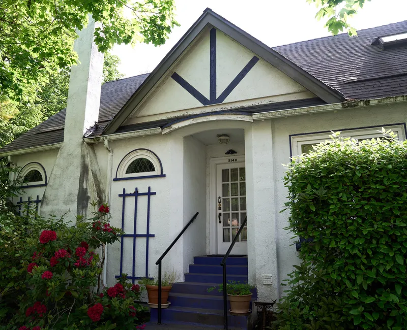 A tan house surrounded by green hedges.