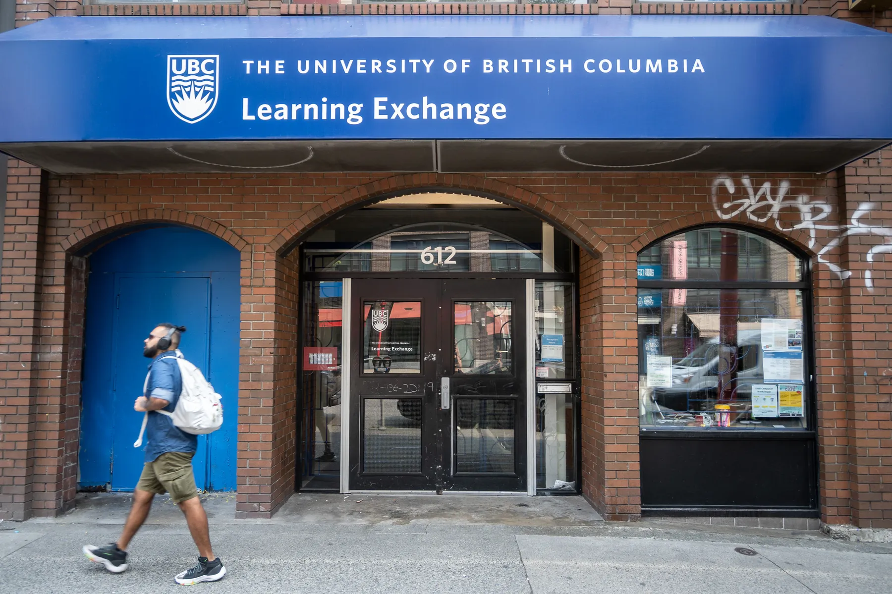 A photo of the Learning Exchange's current location at 612 Main Street in Vancouver's downtown East-side, with a person wearing green shorts and a blue shirt walking across from the entrance.