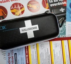 A photo of a naloxone kit over overlapping posters talking about dealing with overdoses.