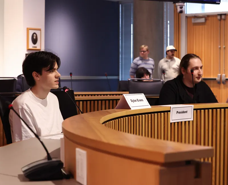 Two people sit a wooden round tables.