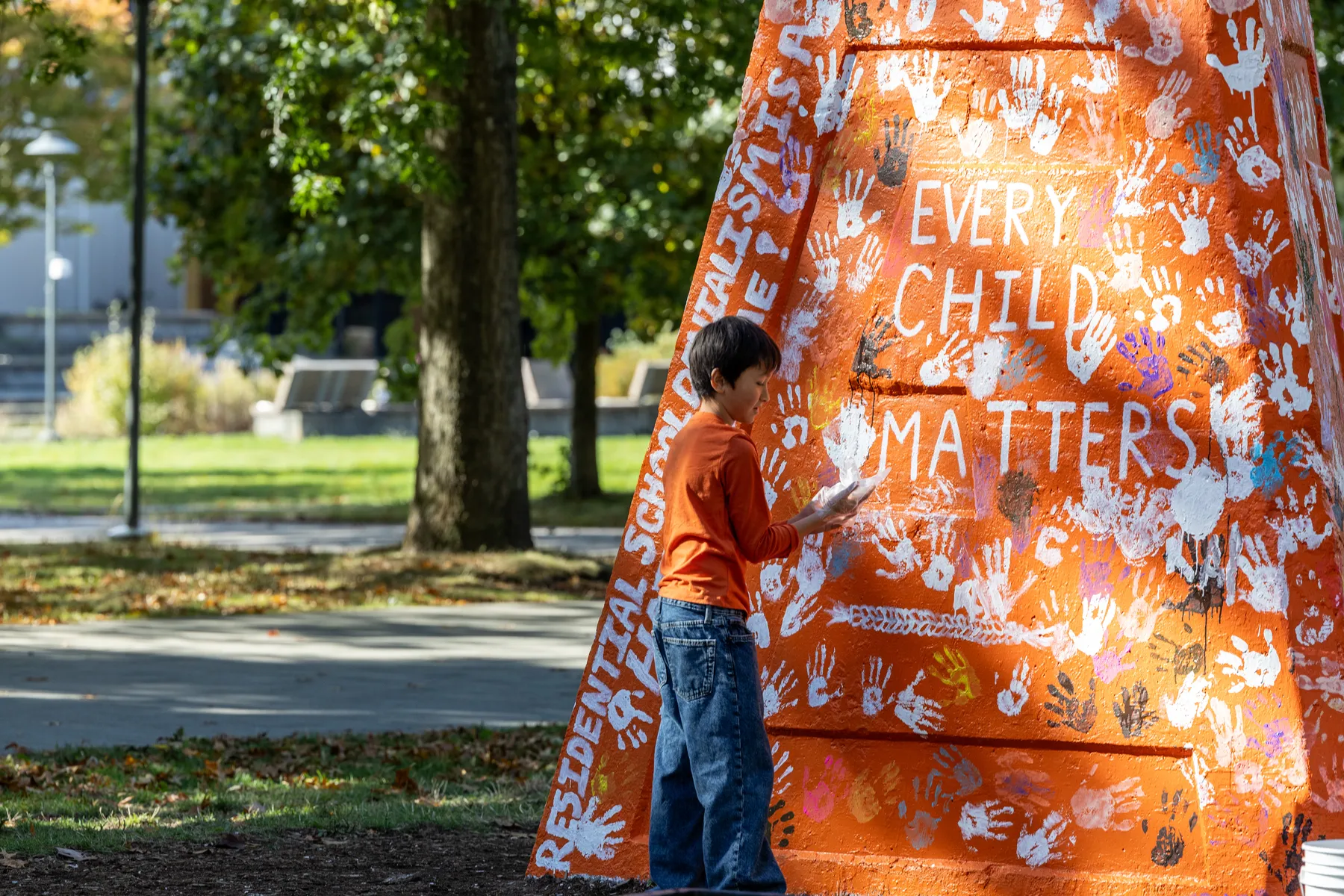 A photo of a child placing a hand print on the Engineering cairn, which was painted orange for the event and read: "Every Child Matters" and "Residential School denialism is a hate crime!"
