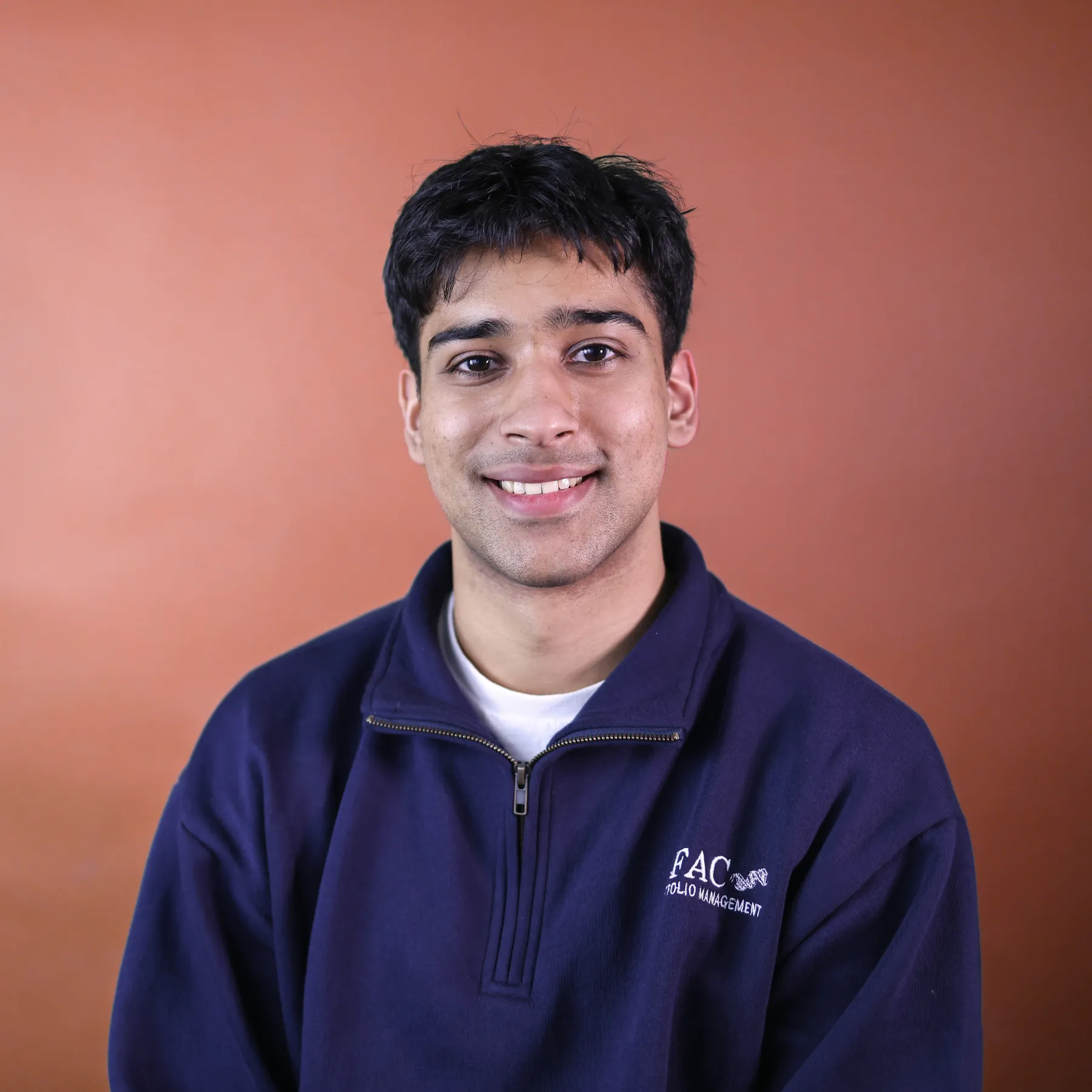 Against an orange background, a man smiles at the camera.