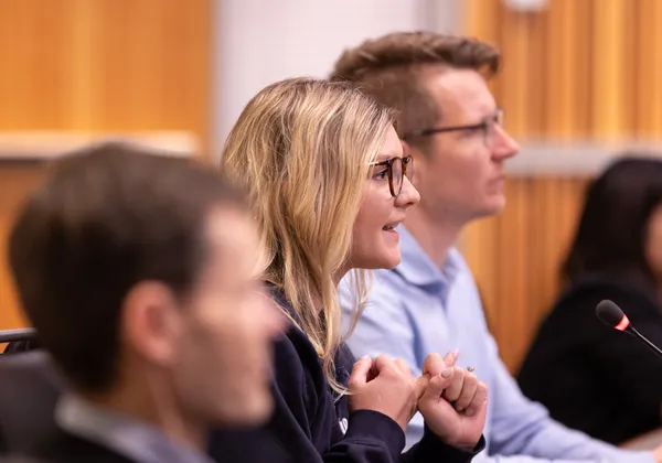 A women speaks into a microphone between two men in a row.