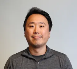 A man in an dark grey shirt looking straight ahead with a white background.
