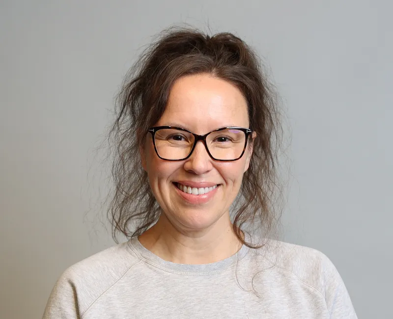 Photo of a woman in a light grey sweatshirt facing the camera with a blank background.