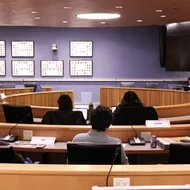 Inside a meeting room, several people sit and discuss.