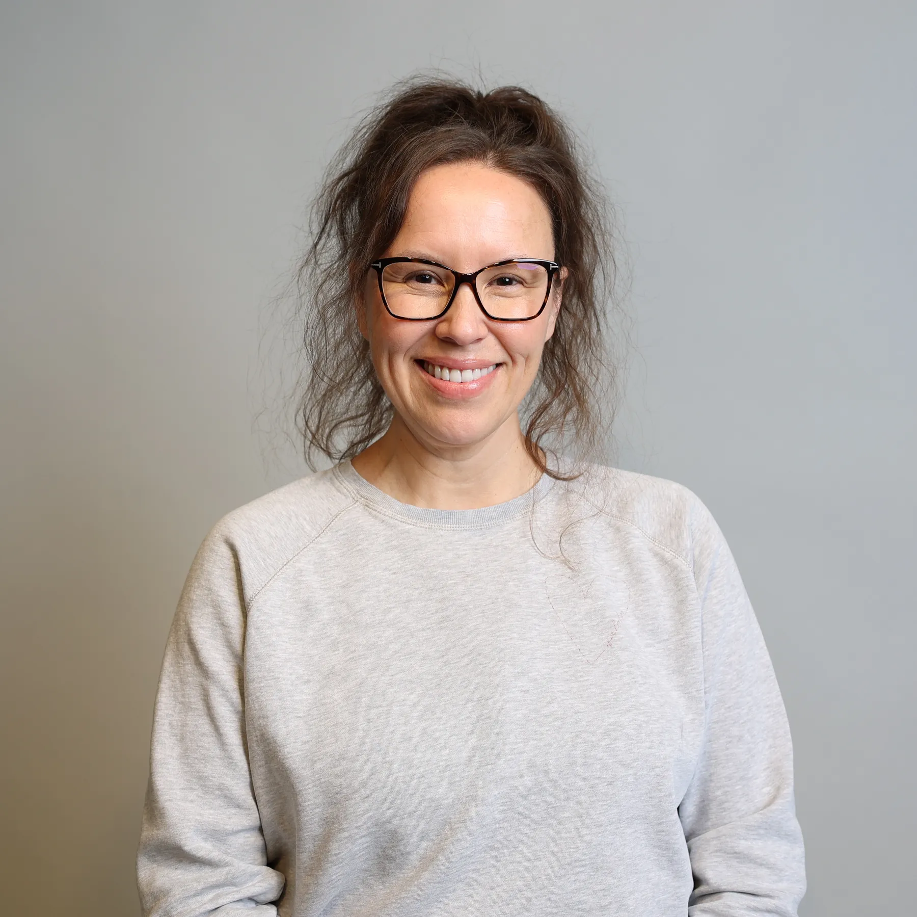 Photo of a woman in a light grey sweatshirt facing the camera with a blank background.