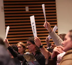 Numerous people sitting down raise their placards in a room.