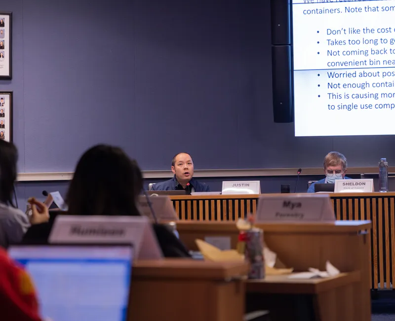Inside a room, a man gives a presentation to councillors.