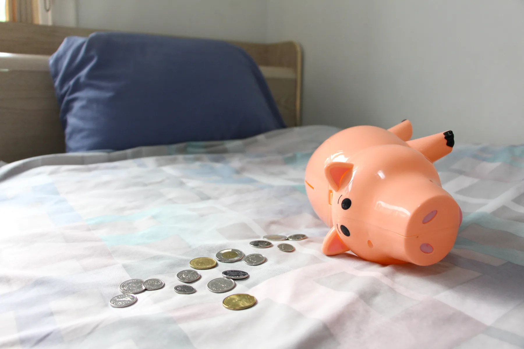 Inside student housing, a piggy bank and coins are strewn across a bed.