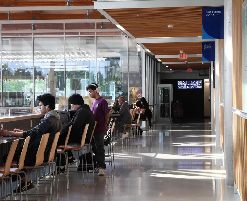 On an upper floor of the AMS Student Nest, students study at desks overlooking the main atrium. In the hallway are AMS signs.