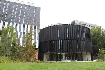 A large, round, black building sits in a grassy area. Pictured is the Arts Student Centre.