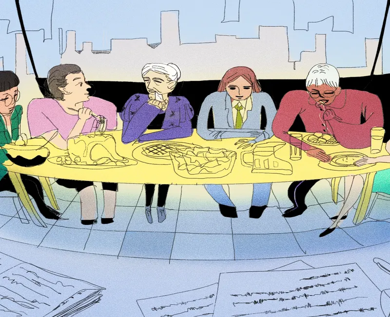 Group of people in office sitting around a long table eating a meal. In the foreground, pen and paper are laid on a table.