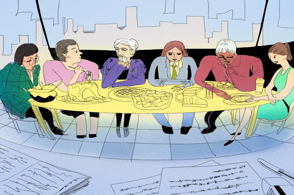 Group of people in office sitting around a long table eating a meal. In the foreground, pen and paper are laid on a table.