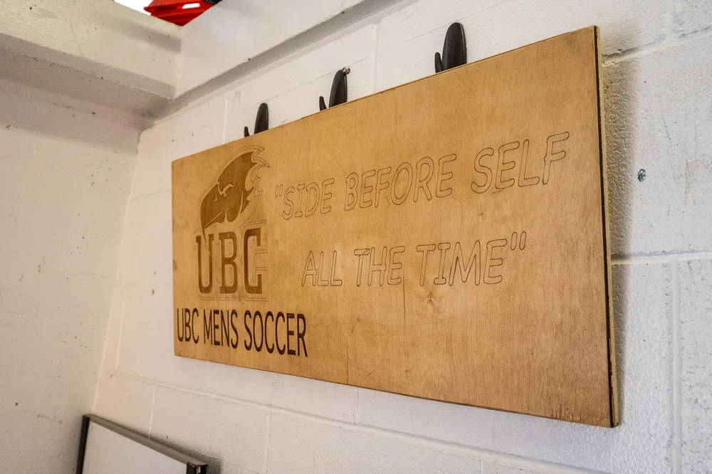 A sign on the wall of the men's team's locker room that reads "Side over self, all the time."