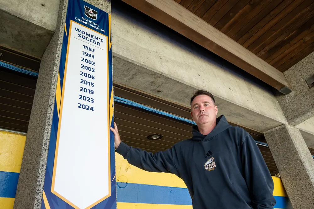 Symons stands next to the banner at Thunderbird Stadium that lists the women's team's national titles.