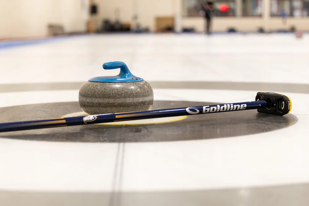 A curling stone and a broom laying on the ice.